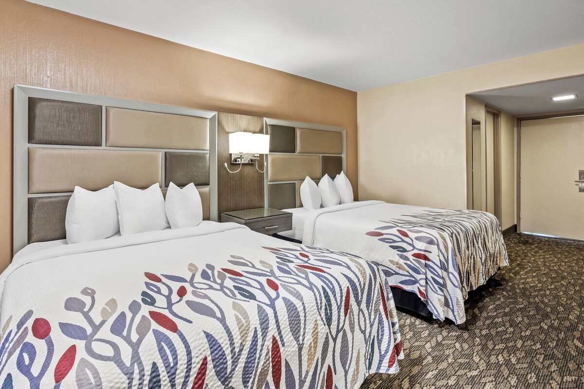 Una habitación de hotel con dos camas, una mesita de noche, una lámpara y piso alfombrado.