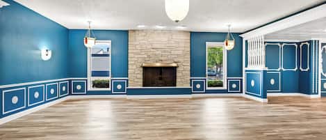 Una habitación amplia con chimenea de piedra, suelo de madera y paredes azules con molduras decorativas.