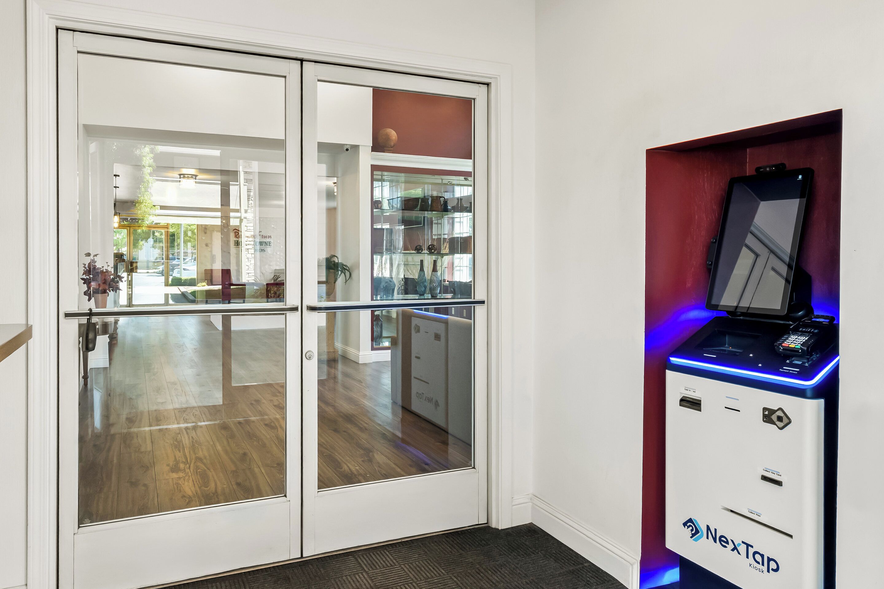 Ein modernes Hotelzimmer mit Glastür zu einem großzügigen Bereich, einem NexTap-Automaten und einer sichtbaren Küchenzeile.
