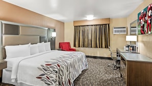 A hotel room with a large bed, a desk, a chair, and a TV on the wall.