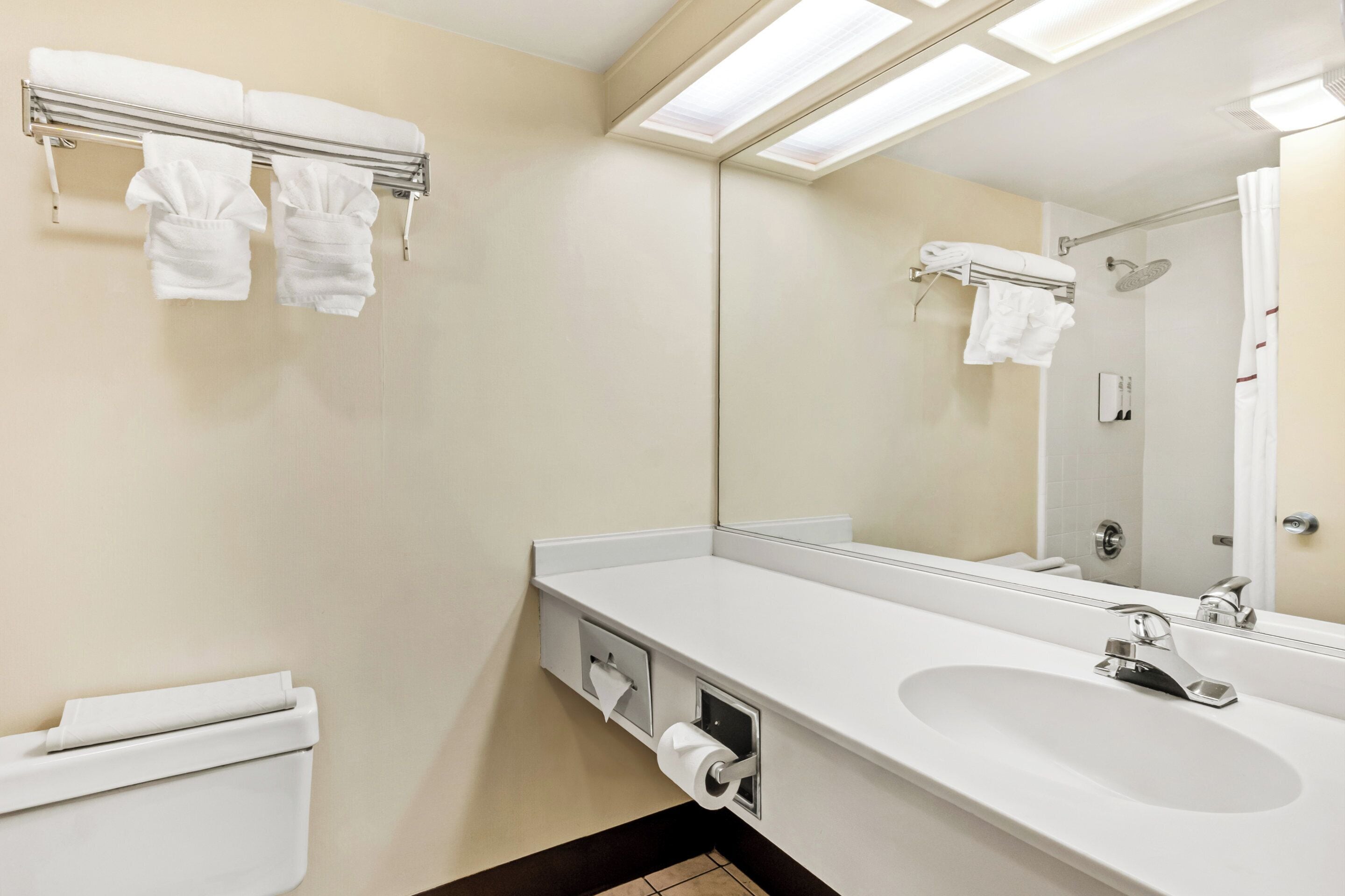 Un baño moderno con un lavamanos blanco, un espejo y un perchero con dos toallas.