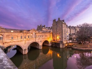 A stone bridge over a calm river, reflecting nearby buildings and trees.