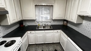 A kitchen with white cabinets, a black countertop, a stainless steel sink, and a white stove. - Refined Home w/Game Room & Large Lounge (Westworth Village)
