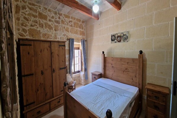 A bedroom with a wooden bed, a wooden wardrobe, and a stone wall.