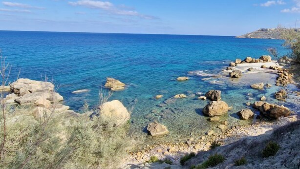 A coastal landscape with clear blue water, rocky shore, and sparse vegetation. - The old Mill (Xaghra)