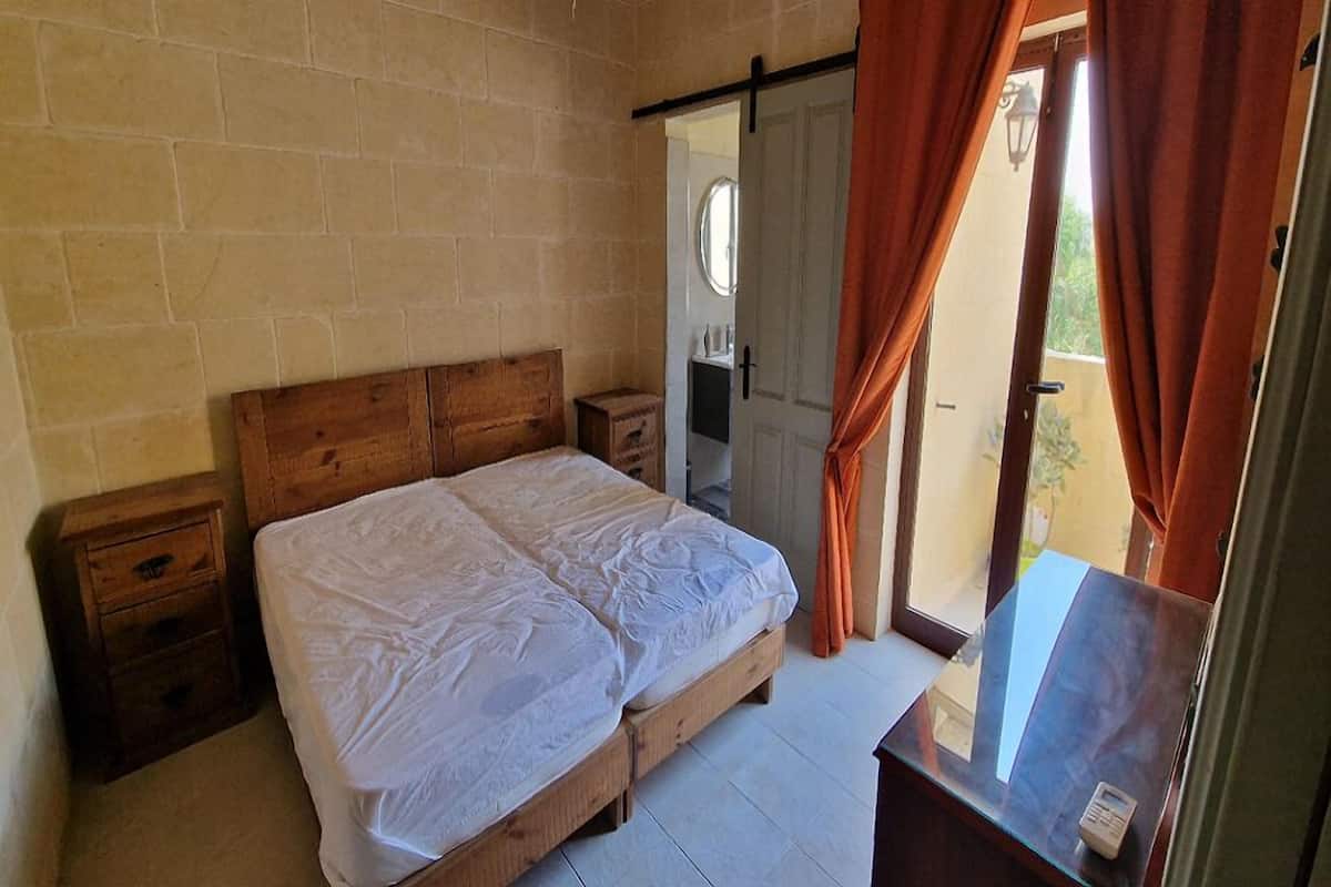 A bedroom with a wooden bed, a nightstand, a mirror, and a sliding door leading to a balcony.