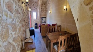 A stone-walled room with a wooden table and chairs, a small cabinet, and a shelf with items. - The old Mill (Xaghra)