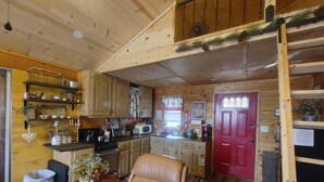 A wooden cabin interior with a kitchen, dining area, and a red door.