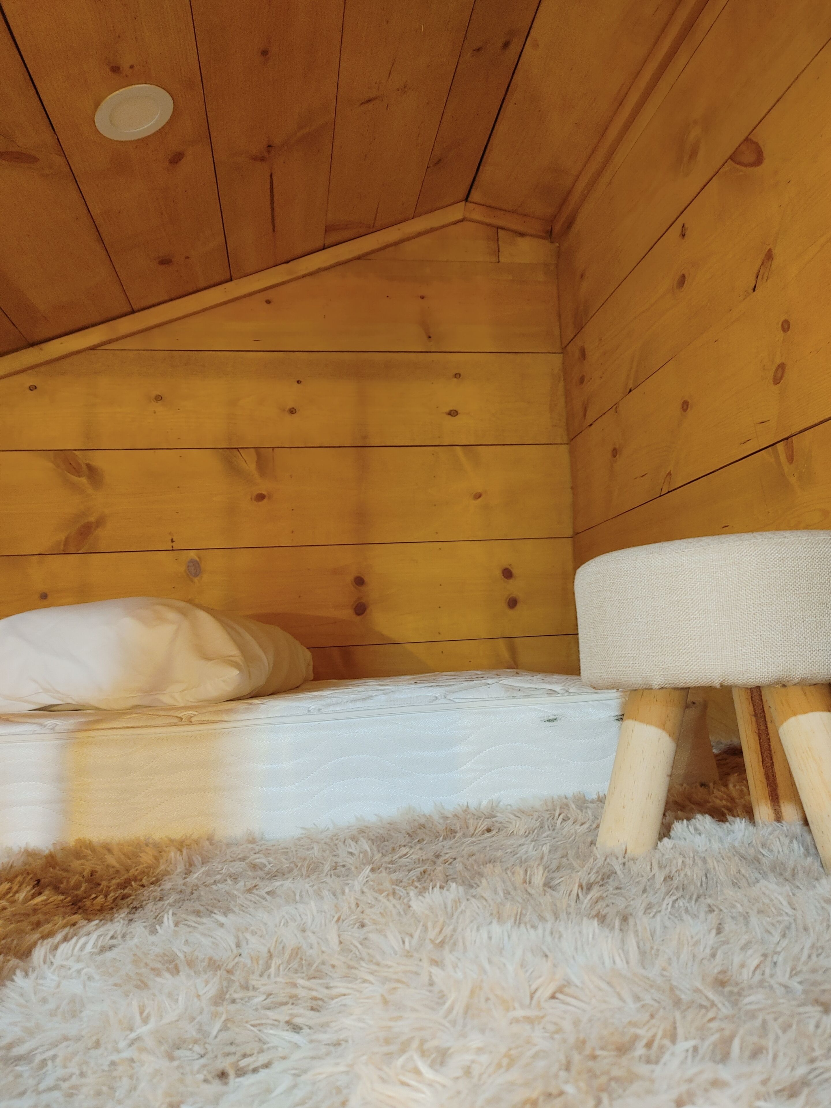 Un interior de madera con una cama, una alfombra mullida y un taburete pequeño de madera.