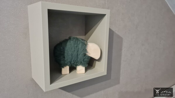 Un estante pequeño, blanco y adherido a la pared, con un borrego de peluche verde oscuro.