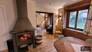 Una habitación acogedora con una estufa de leña, una mesa de comedor y vistas al exterior a través de amplios ventanales.