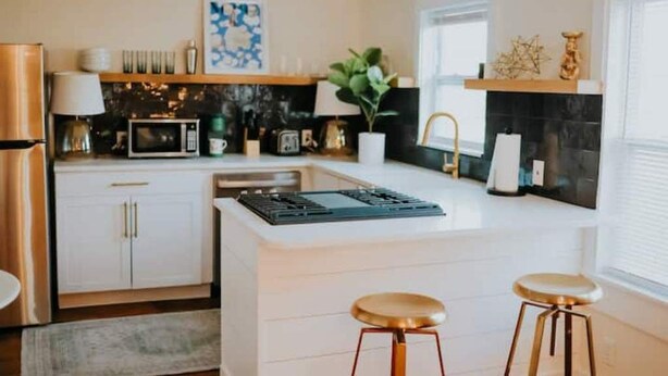 Una cocina moderna con armarios blancos, una isla central con taburetes, microondas y estufa.
