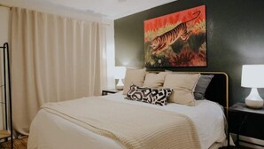 Un dormitorio con cama, mesita de noche, lámpara, un cuadro de un tigre y un ventilador de techo.