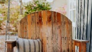 Asiento de madera rústico con cojín, colgado de una cadena, ubicado al aire libre.