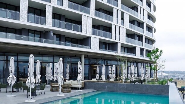 Ein modernes Hotel mit großzügiger Poolanlage, Außenbereich zum Sitzen und Blick auf die Skyline.