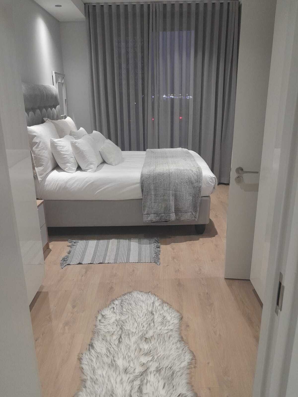 A modern bedroom with a bed, grey curtains, and a view of the city at night.