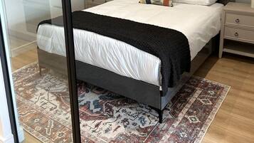 Un dormitorio moderno con una cama grande, mesitas de noche, una alfombra y arte abstracto en la pared.