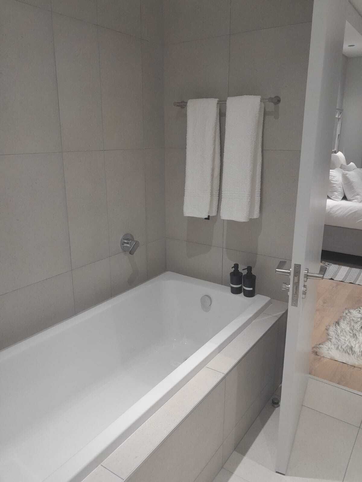 Een moderne badkamer met een bad, twee handdoeken aan een rek en een fles shampoo ernaast.