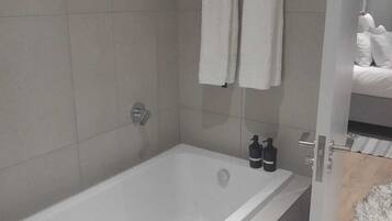 A modern bathroom with a bathtub, two towels hanging on a rack, and a bottle of shampoo on the side.