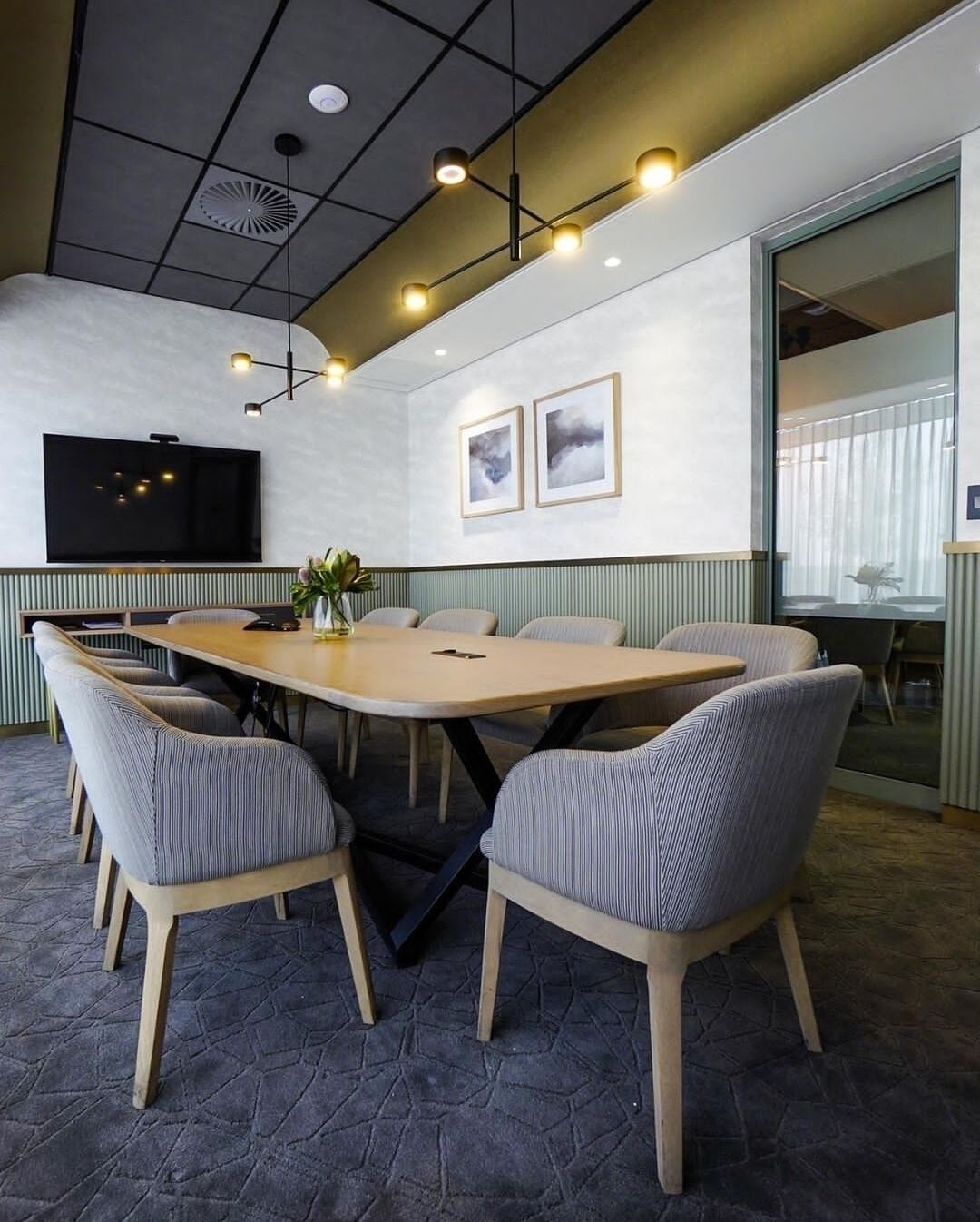 A conference room with a large table and six chairs, a flat-screen TV, and framed artwork on the wall.