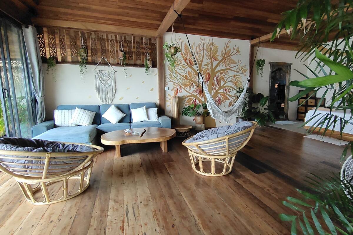 A cozy living area with a wooden ceiling, a blue sofa with patterned cushions, wicker chairs, and a round wooden coffee table.