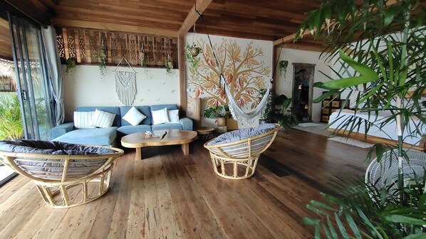 A cozy living area with a wooden ceiling, a blue sofa with patterned cushions, wicker chairs, and a round wooden coffee table. - Whynam Beach (Ko Pha-ngan)
