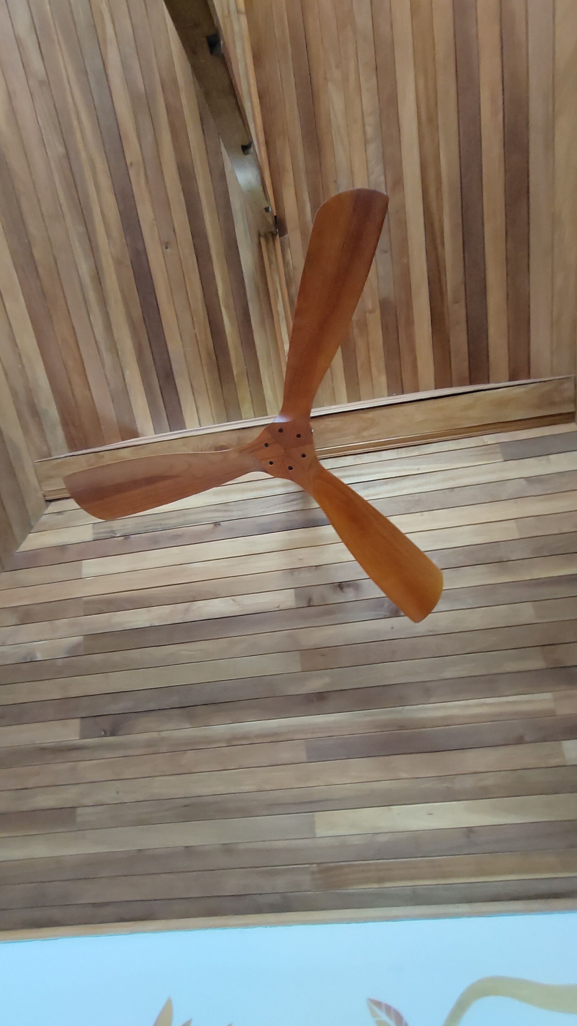 Een plafondventilator met houten afwerking in een kamer met houten lambrisering.