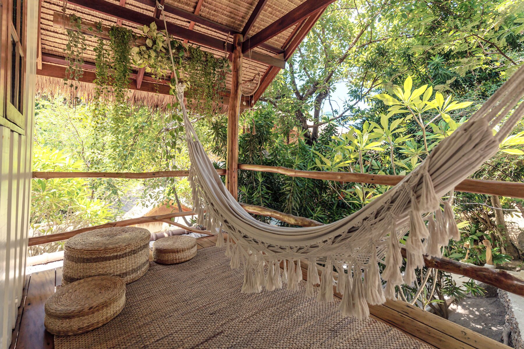 A hammock suspended from a wooden structure with woven mats on the floor.