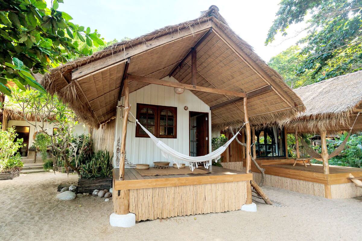 A rustic hut with a thatched roof, a hammock, and a wooden deck.