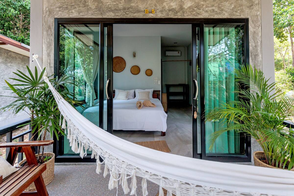 A modern bedroom with a large bed, a hammock, and potted plants.