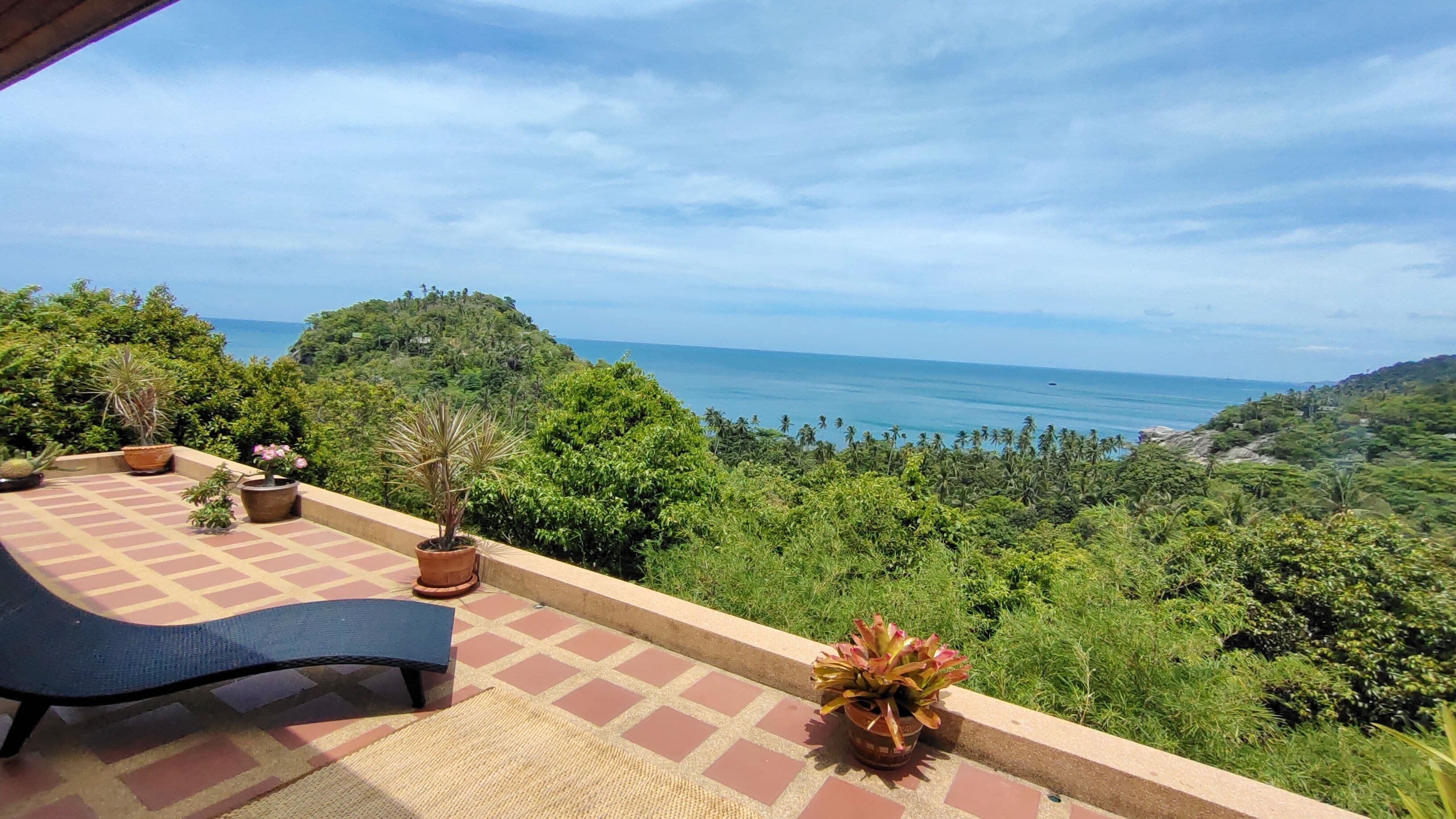 Una terraza con vista al mar, plantas en macetas y una silla de descanso.