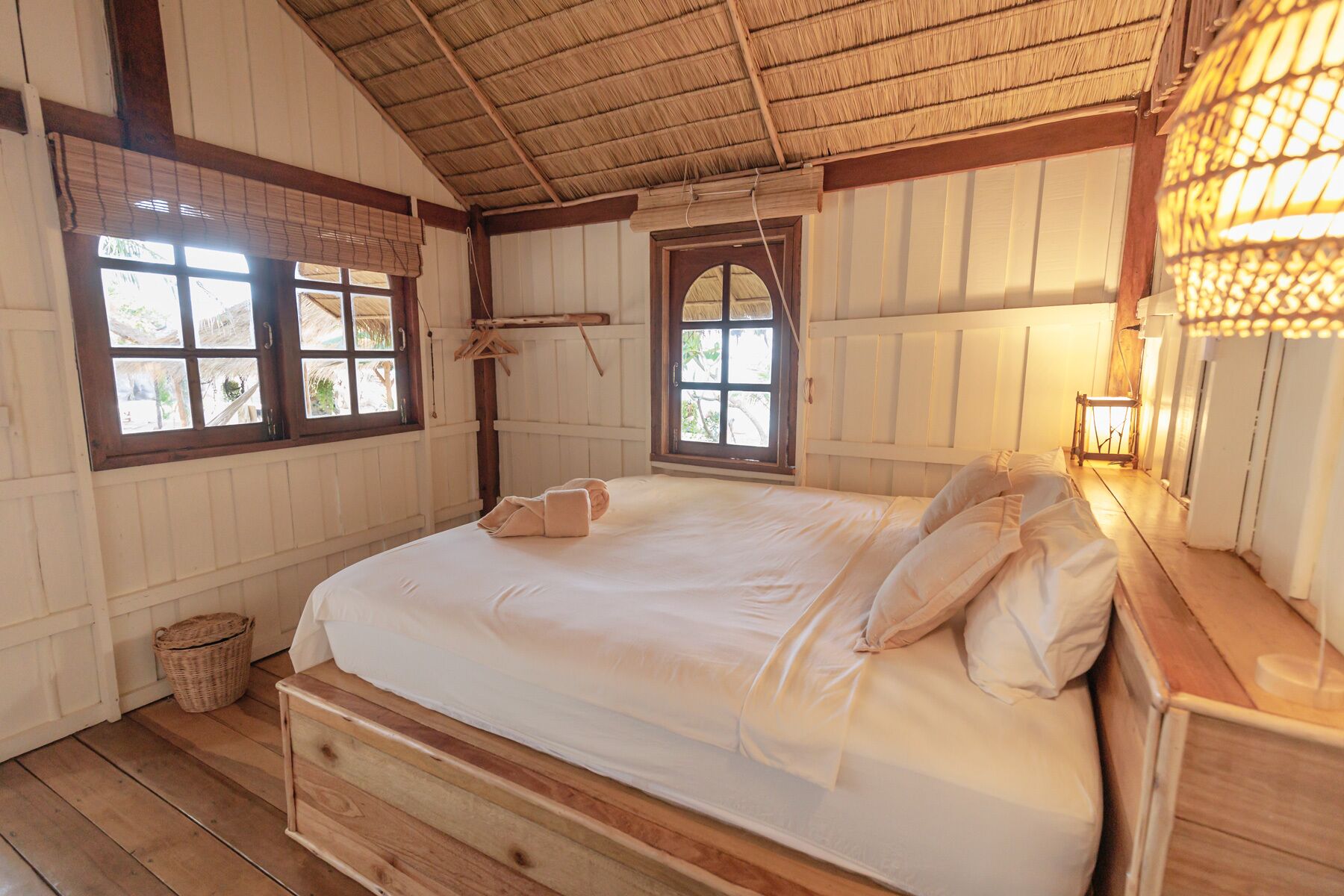 A room with a wooden bed, two windows, a hanging light fixture, and a woven basket.