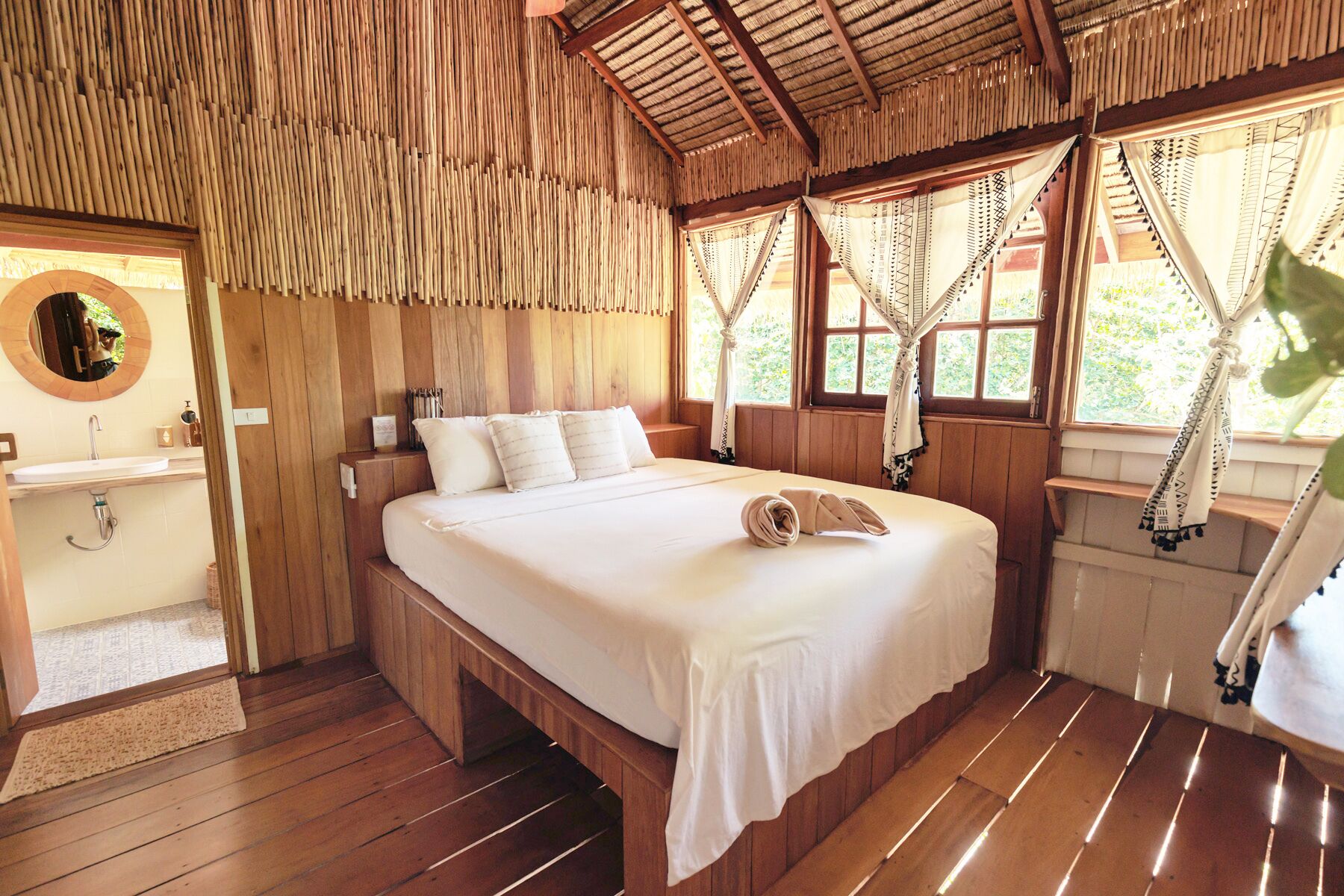 A wooden room with a bed, a sink, and windows with curtains.