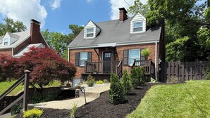 A two-story house with a brick exterior, a front porch, and a small garden area with mulch and plants.