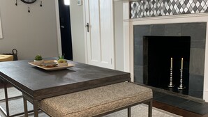 A dining area with a dark wooden table, bench, and patterned rug. A fireplace with two candles is visible in the background.
