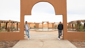 Two men standing under a large archway with a pool in the background.