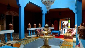 A traditional Moroccan interior with a fountain, tiled floors, and blue and red decor.