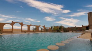 A swimming pool with circular stepping stones, a desert landscape, and a clear blue sky.