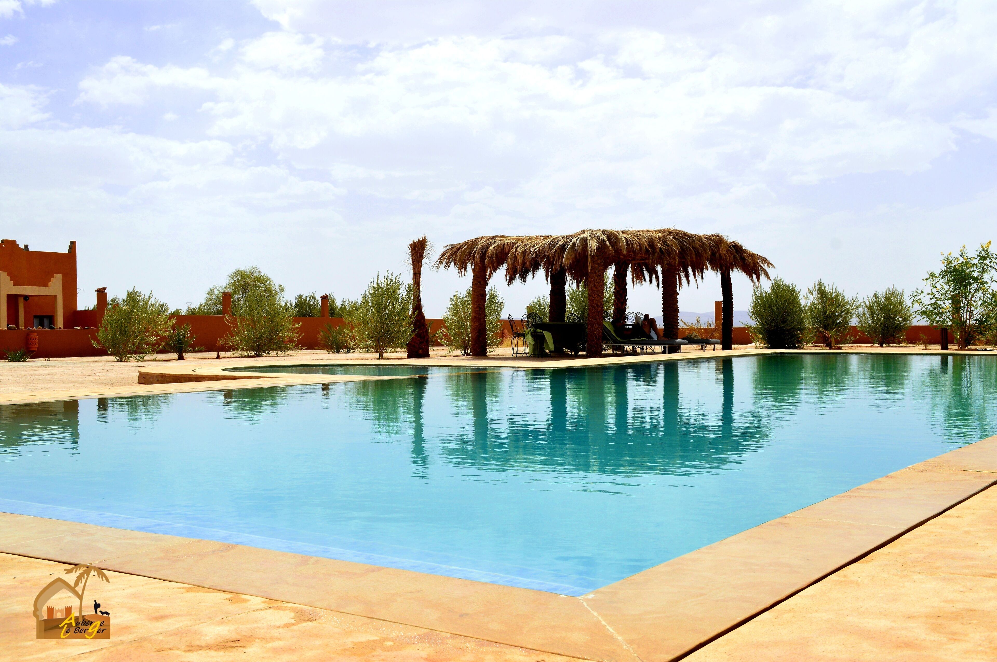 Una piscina con techo de paja, palmeras y cielo despejado.