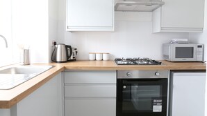 Une cuisine moderne avec des meubles blancs, une cuisinière à gaz en acier inoxydable, un four encastré, un four à micro-ondes et un évier.