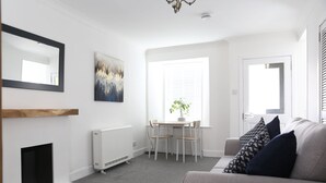 Un salon moderne avec une cheminée, un coin repas avec une table et des chaises, et une grande fenêtre avec des stores.