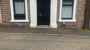 Un bâtiment avec une porte noire et deux fenêtres dotées de volets.
