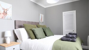 Une chambre à coucher avec un lit, des oreillers, une table de chevet, une lampe et une porte.