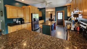 A kitchen with granite countertops, wooden cabinets, a stainless steel refrigerator, and a ceiling fan. - Lake George 6 Bedroom Home lake access (Lake George)