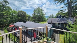 A deck with a railing overlooking a dining area and a building with a dark roof. - Lake George 6 Bedroom Home lake access (Lake George)