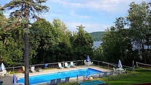 A rectangular swimming pool with lounge chairs and umbrellas, surrounded by trees and a view of a lake. - 2 Bed /2 bath cabin w/ Lake George access (Lake George)