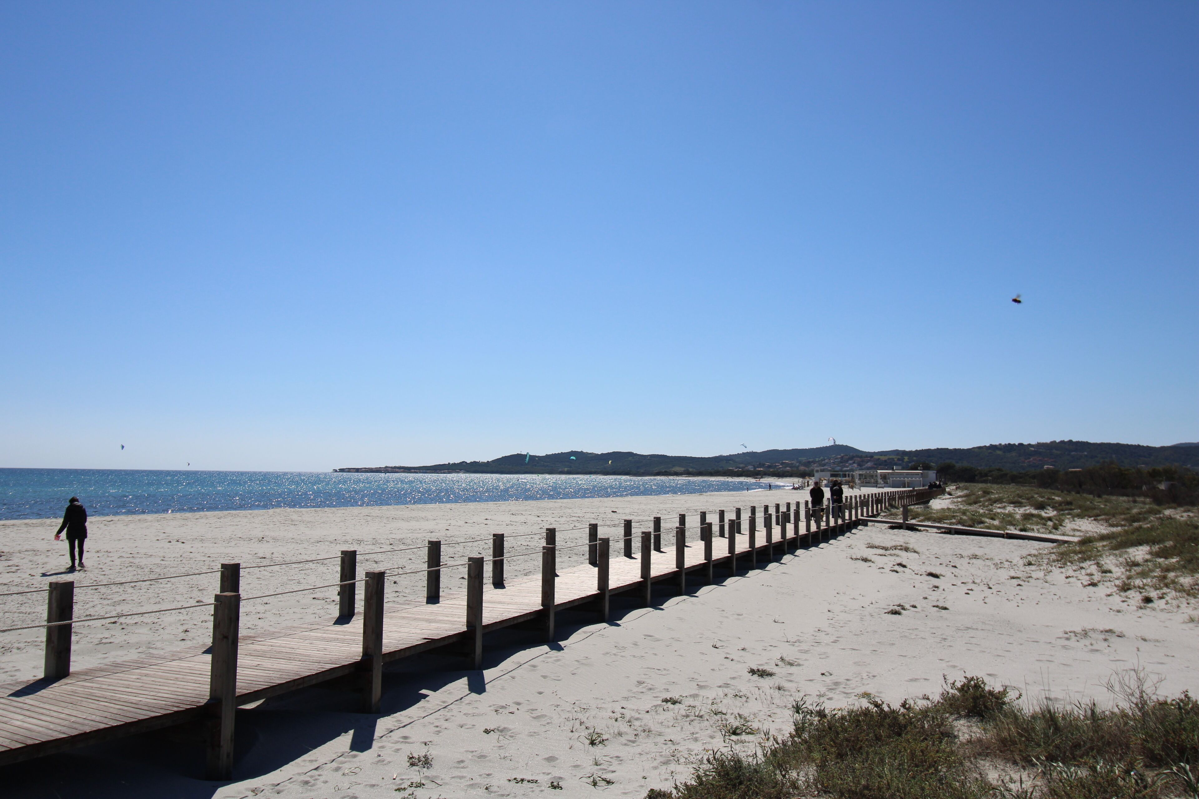 Une plage avec une promenade en bois qui mène à l’eau, un terrain sablonneux et des collines à l’horizon.