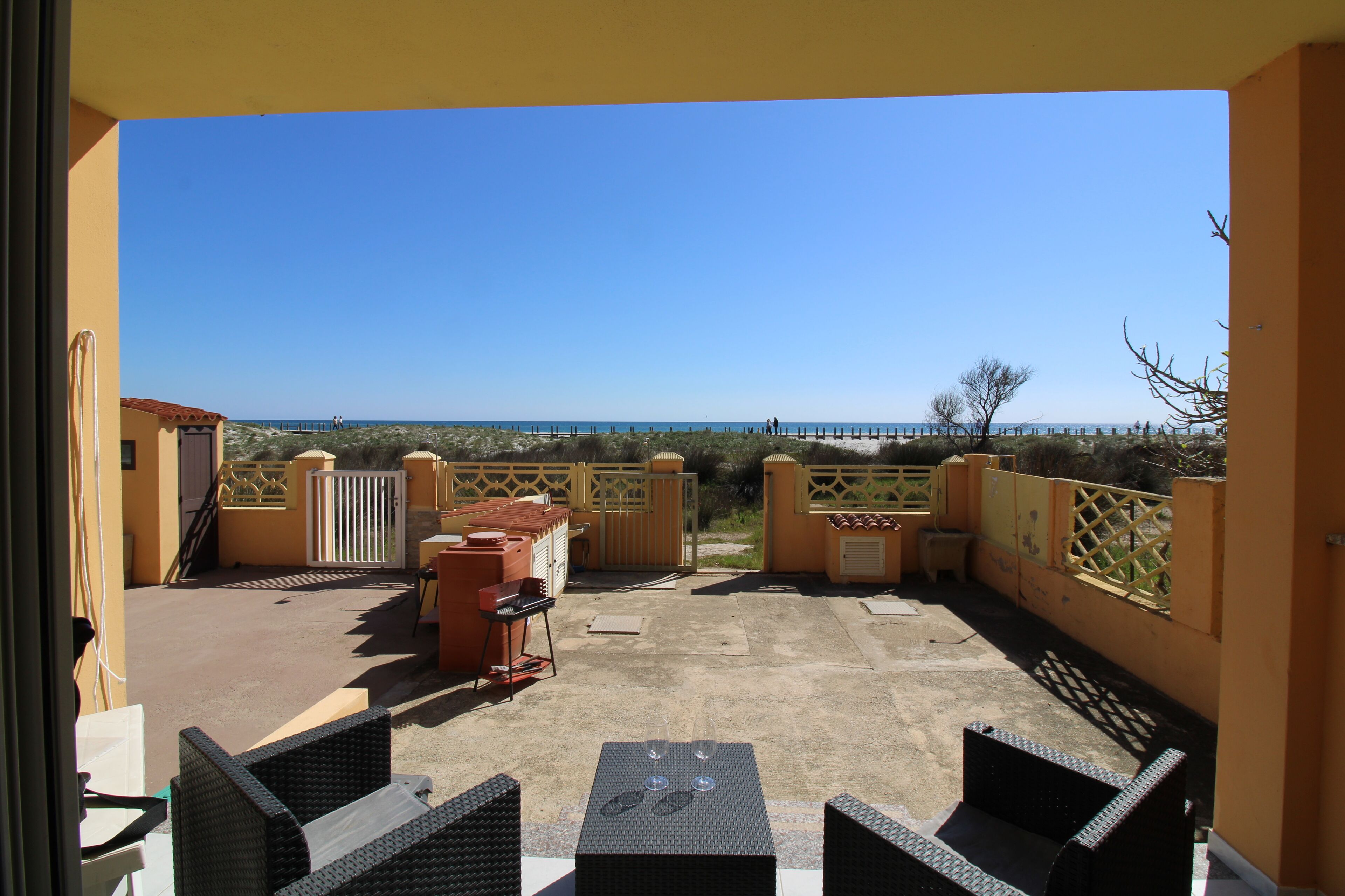 A balcony with wicker furniture, a table with glasses, and a view of the beach and ocean.
