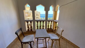 Un balcón con una mesa y dos sillas, con vistas a una zona costera con edificios y el mar.