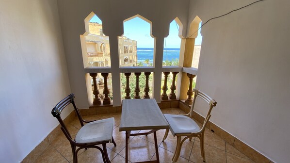 A balcony with a table and two chairs, overlooking a coastal area with buildings and the sea.
